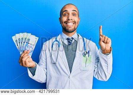 Hispanic adult doctor man wearing medical uniform holding 100 south african rand smiling with an idea or question pointing finger with happy face, number one 