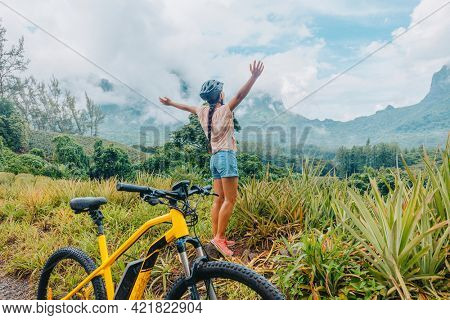 Mountain e biking happy girl with arms up of happiness traveling on Tahiti island with e-bike riding electric mtb bicycle on trail adventure. Travel summer lifestyle.