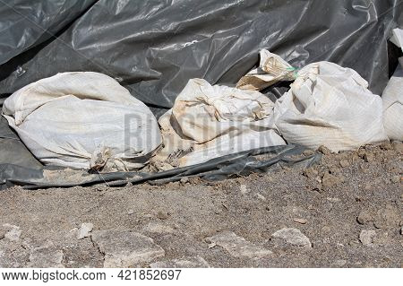 Row Of New And Old Broken White Sandbags Holding Thick Dark Nylon Protection Covering Temporary Floo