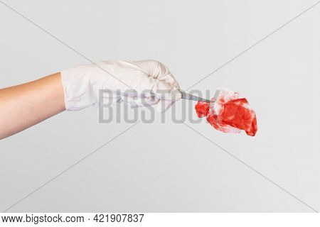 Gloved hand using tweezers to hold a red gauze