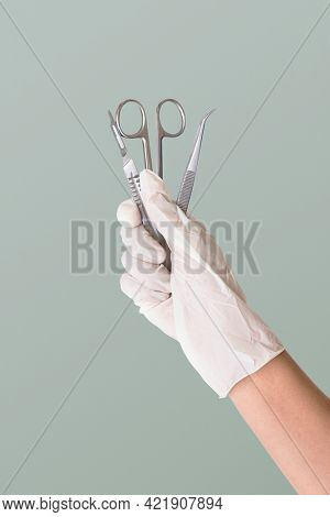 Gloved hand holding stainless steel medical instruments
