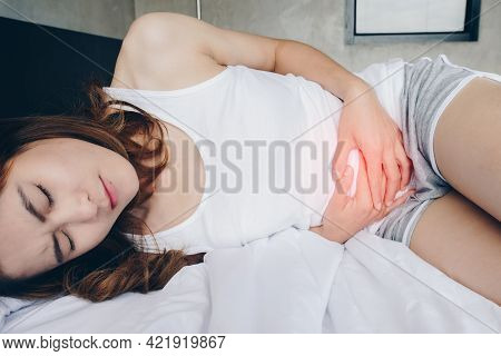 Portrait Of Asian Woman Having Painful Stomachache On Bed. Conceptual Of Woman Suffering Stomach Ach