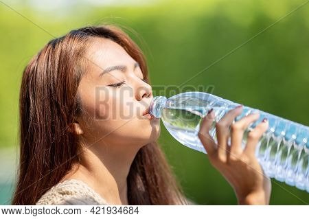 Asian Woman Drinks Big Bottle Water In Outdoor Green Bokeh Tree Background.