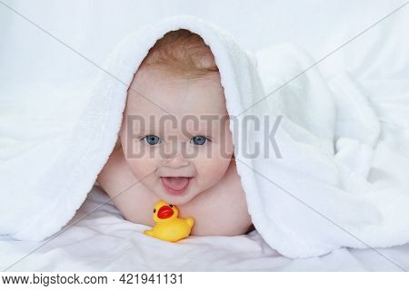 A Smiling Toddler, Covered With A Towel, Dries Off After Bathing And Plays With A Multi-colored Toy 