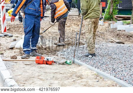 Road Workers Use Shovels To Prepare A Sandy Foundation On A Sidewalk And Cover It With Rubble Along 
