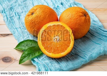 Ripe Sweet Juicy Oranges On A Turquoise Cloth Over Wooden Table. Two Whole And One Half Of Fresh Cit