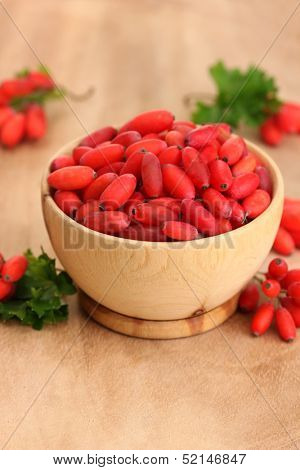 ripe barberries in wooden bowl with green leaves, on table