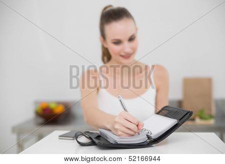 Smiling young woman writing in a planner in the kitchen at home