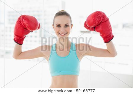 Sporty smiling woman holding up boxing gloves in bright room