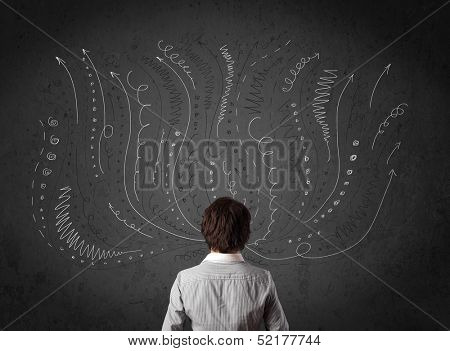 Thoughtful young businessman standing and deciding in front of a chalkboard with sketched arrows and lines in different directions