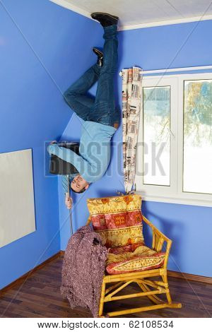 Man in jeans standing on the ceiling holding a lamp