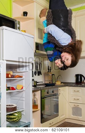 Mother with son stand upside down in the kitchen with fridge