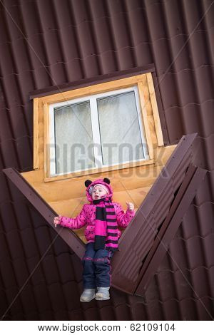 Little girl sitting on the brown roof of the upside-down house
