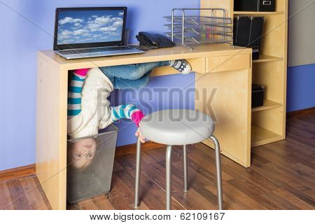 Little girl in jeans under the table with head in basket at inverted house