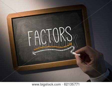 Hand writing the word factors on black chalkboard
