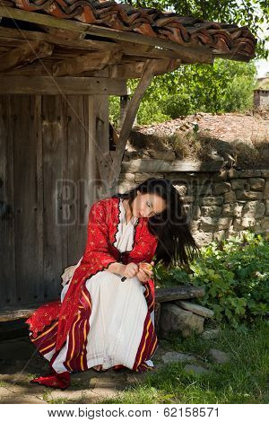 Beautiful woman in bulgarian dress peeling an apple in the old village of Jeravna