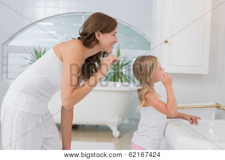 Side view of a little girl brushing teeth with mother in the bathroom