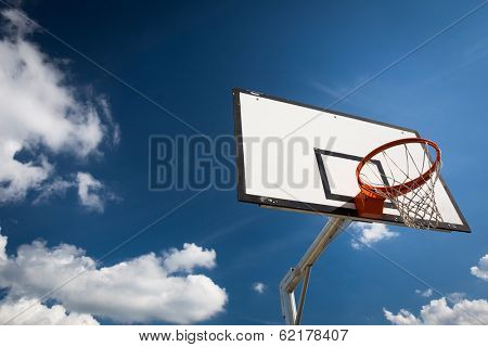 Basketball hoop against  lovely blue summer sky with some fluffy white clouds