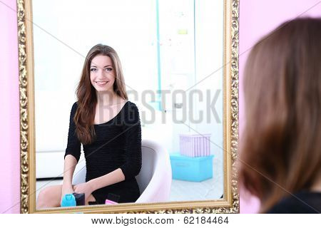 Young beautiful woman sitting front of mirror in room