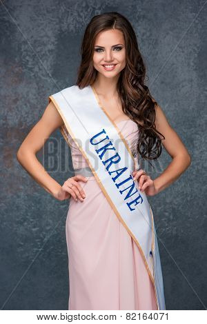 Beautiful young brunette woman with her hair posing in a i long dress. Studio, on gray background