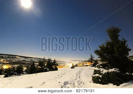 moon shining on a snowy hills and tree with luminous city