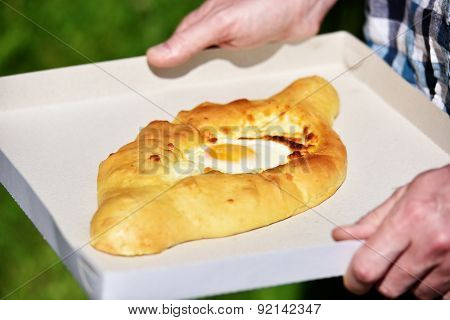 Man holding a paper box with Adjarian khachapuri, the traditional gondola shaped bread with egg