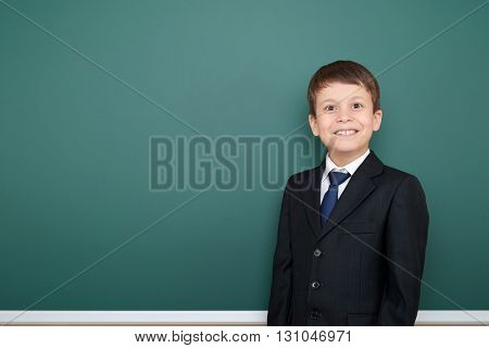 happy successfull school boy in black suit portrait on green chalkboard background, education concept