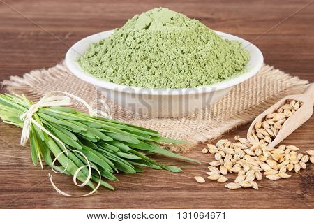 Young powder barley in glass bowl barley grass and grain on jute canvas wooden background healthy nutrition and lifestyle body detox