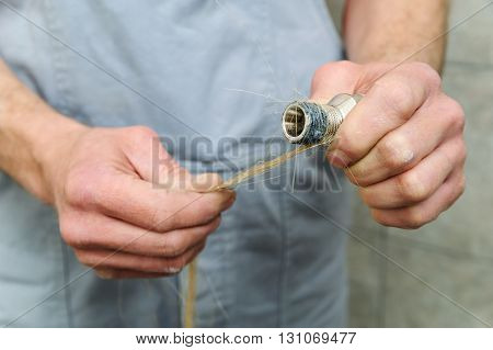 Plumber putting hemp fibers on a thread pipe.