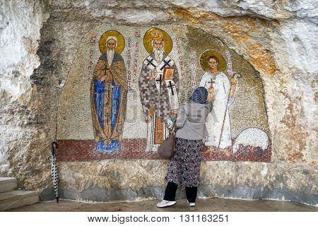 OSTROG MONTENEGRO - May 15 2016: unidentified woman prays at the Mosaics Wall paintings in Serbian Orthodox Ostrog monastery Montenegro. Ostrog is the most popular pilgrimage place in Montenegro.
