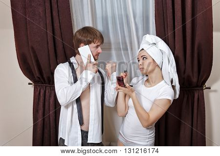 Morning couples. Husband and wife are going to work. Man talking on the phone and asks the girl to hurry. Girl doing make-up with a towel on her head.