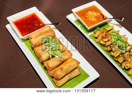 Vegetables spring roll and chicken satay barbecue and sauce on white plate.