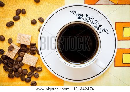Cup of black coffee, brown sugar and coffee beans on a bright orange tablecloth