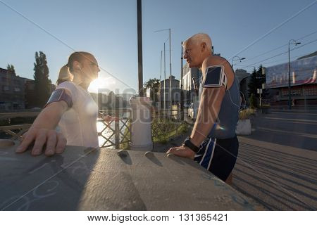 jogging couple check music playlist on phone and plan route before morning running workout  with sunrise in the city  and sun flare in background