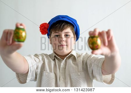 a boy in Russian national cap with cloves holding easter eggs
