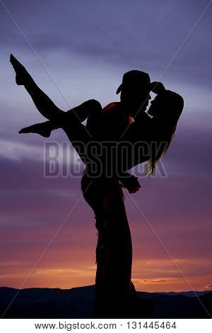 A silhouette of a cowboy holding on to his woman getting ready to kiss.