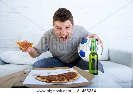 young man watching football game on television celebrating goal crazy happy sitting on sofa couch at home holding and pizza with beer bottle looking excited and cheerfull