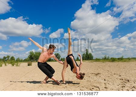 Contemporary dance. Man and woman in passionate dance pose on beach. Young couple dancing modern dance in beautiful pose outdoors. Girl doing splits against the sky clouds. A man with naked torso on sand.
