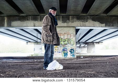 Lost Homeless Man Standing With Bag Under Bridge.