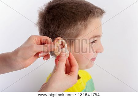 Audiologists hand showing a hearing aid before inserting it into a young boys ear. Focused on the hands and the hearing aid.