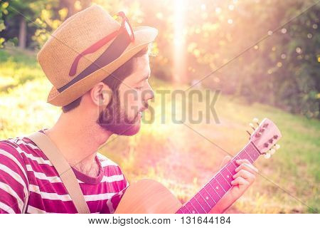 Young man playing guitar in city park on sun rays background - Handsome hippie style guitarist engrossed on music outdoors - Concept of freedom relaxation and passion - Vintage look and sun flare