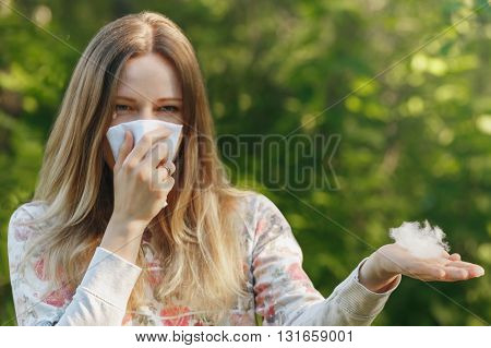 young woman suffering spring pollen allergy. Sneezing into a white handkerchief, holding a sprig with fuzz.