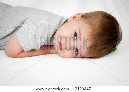 A handsome little boy laying on his stomach with head down on a white background smiles sweetly at the camera.