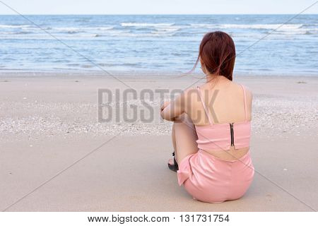 Asian woman sitting on the beach looking at the sea and sky