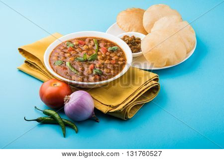 spicy chick peas also known as Chola Masala or Chana Masala or Chole served with fried puri, pickle and green salad
