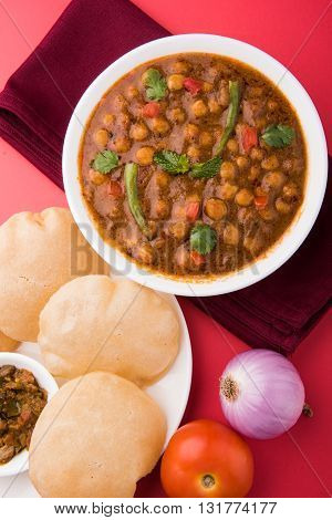 spicy chick peas also known as Chola Masala or Chana Masala or Chole served with fried puri, pickle and green salad