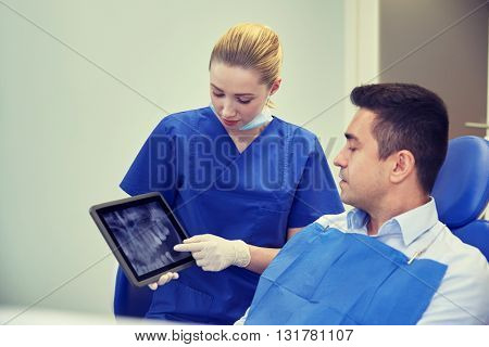 people, medicine, stomatology and health care concept - female dentist showing teeth x-ray scan on tablet pc computer screen to male patient at dental clinic office