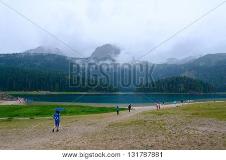 ZABLJAK MONTENEGRO - SEPTEMBER 20 2015: Unidentified tourists visit Black Lake in Durmitor National Park on rainy day Montenegro