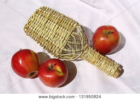 glass bottle under wine weaves willow rods and three red juicy apples