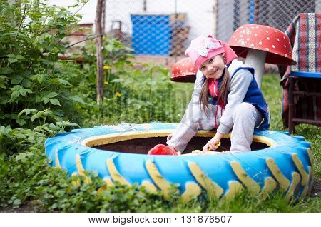 Child girl sitting outdoors in courtyard of kindergarten. Happy kids playing in sand playpit